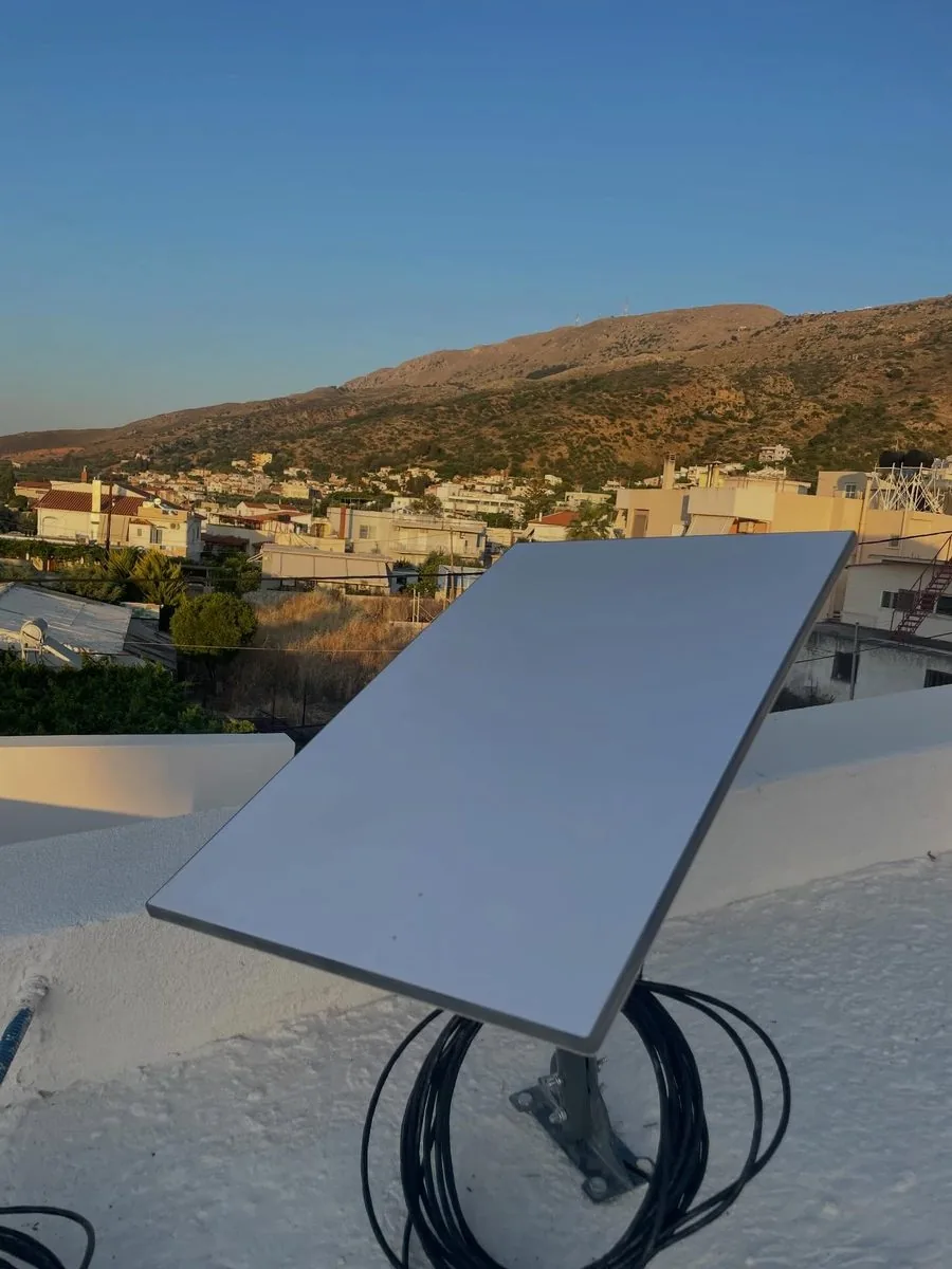Starlink dish mounted on a rooftop at golden hour, overlooking a Cretan village and mountains