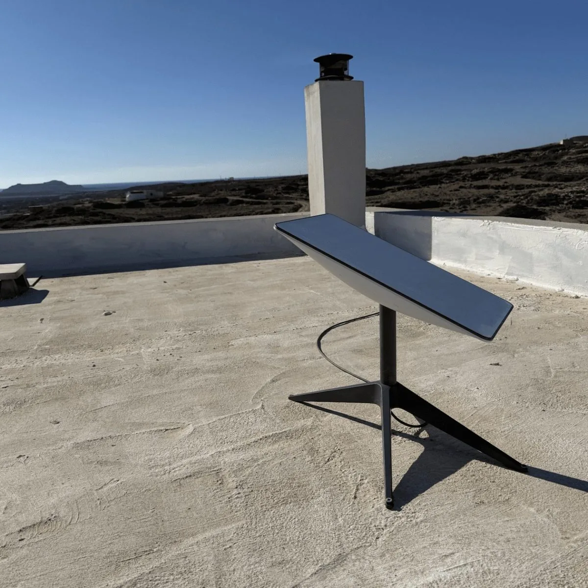Starlink dish installed on a whitewashed rooftop in Crete, with hills and the sea on the horizon