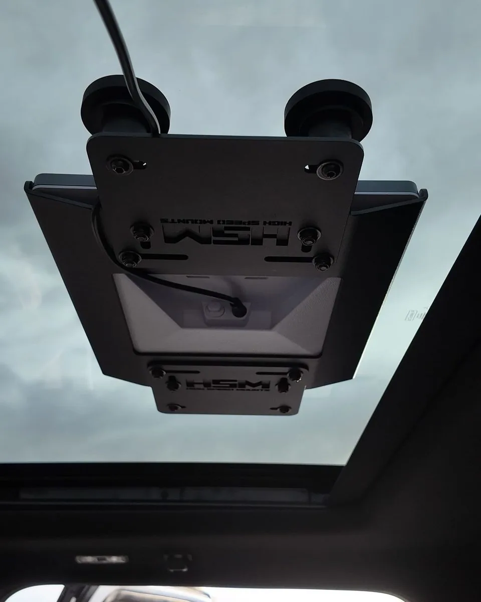 View up through a vehicle sunroof at the suction mounting plate holding a Starlink Mini, cable entering through the sunroof