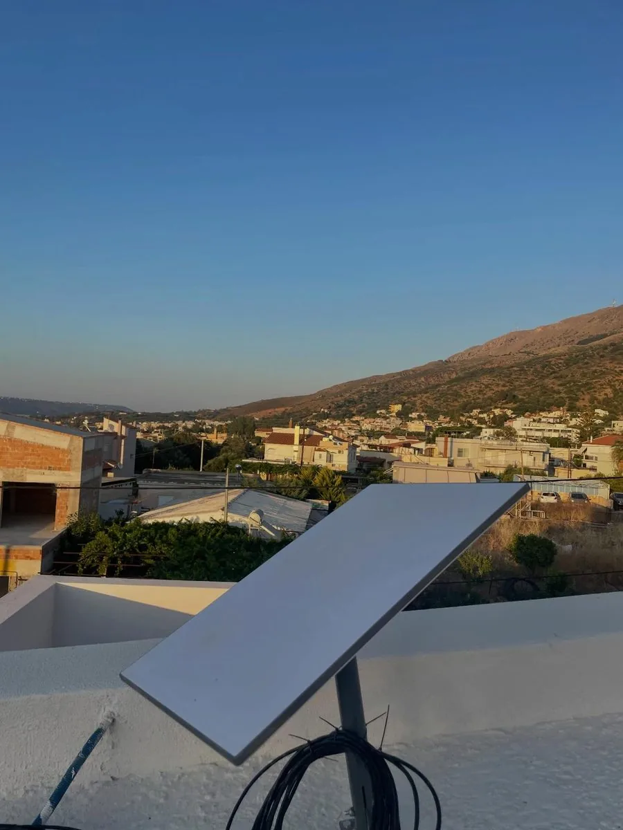 Starlink dish on a wall mount with cabling routed, village and mountain backdrop in Crete